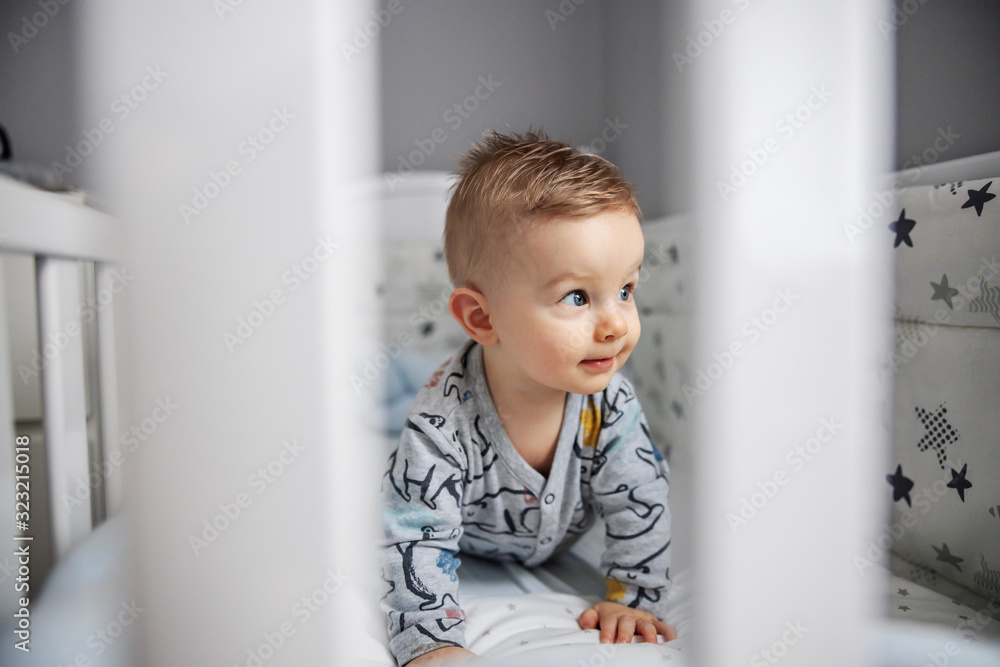 Adorable blond little baby boy lying on stomach in his crib and looking at something interesting. Adorable blond little baby boy lying on stomach in his crib and looking at something interesting.