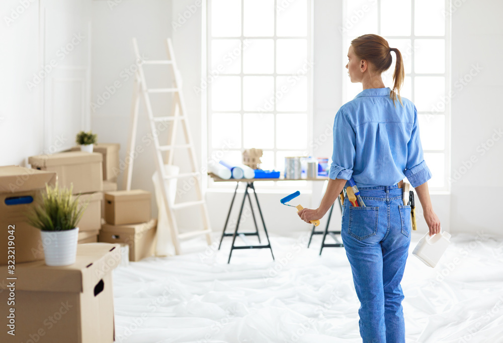 Pretty smilling woman painting interior wall of home with paint roller Pretty smilling woman painting interior wall of home with paint roller
