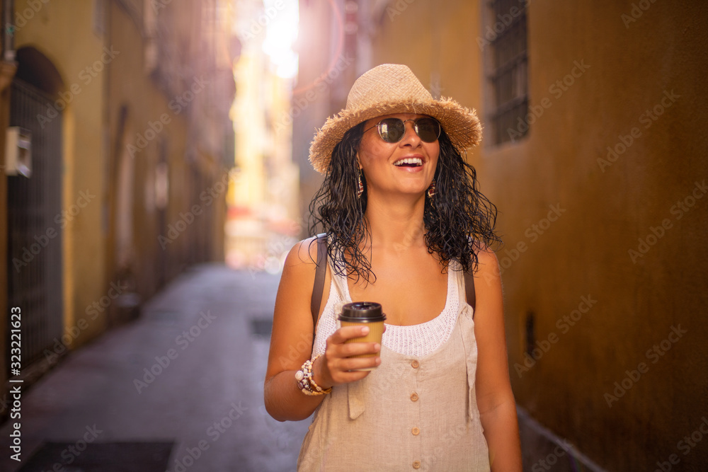  A beautiful woman is walking at the narrow streets of Nice, France.  She is drinking coffee to go