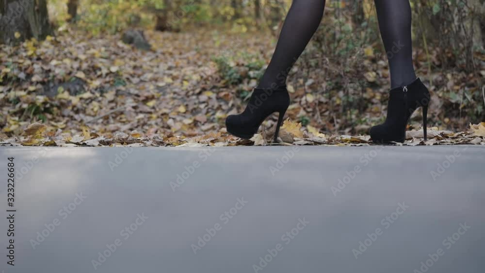 Female legs walking on the road in black tights and shoes with high heels Female legs walking on the road in black tights and shoes with high heels
