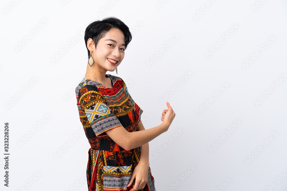 Young Asian girl with a colorful dress over isolated white background pointing back Young Asian girl with a colorful dress over isolated white background pointing back