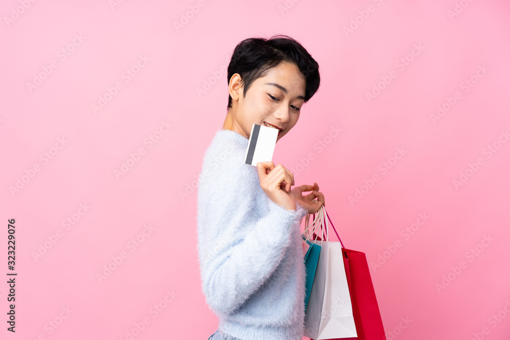 Young Asian girl over isolated pink background holding shopping bags and a credit card Young Asian girl over isolated pink background holding shopping bags and a credit card