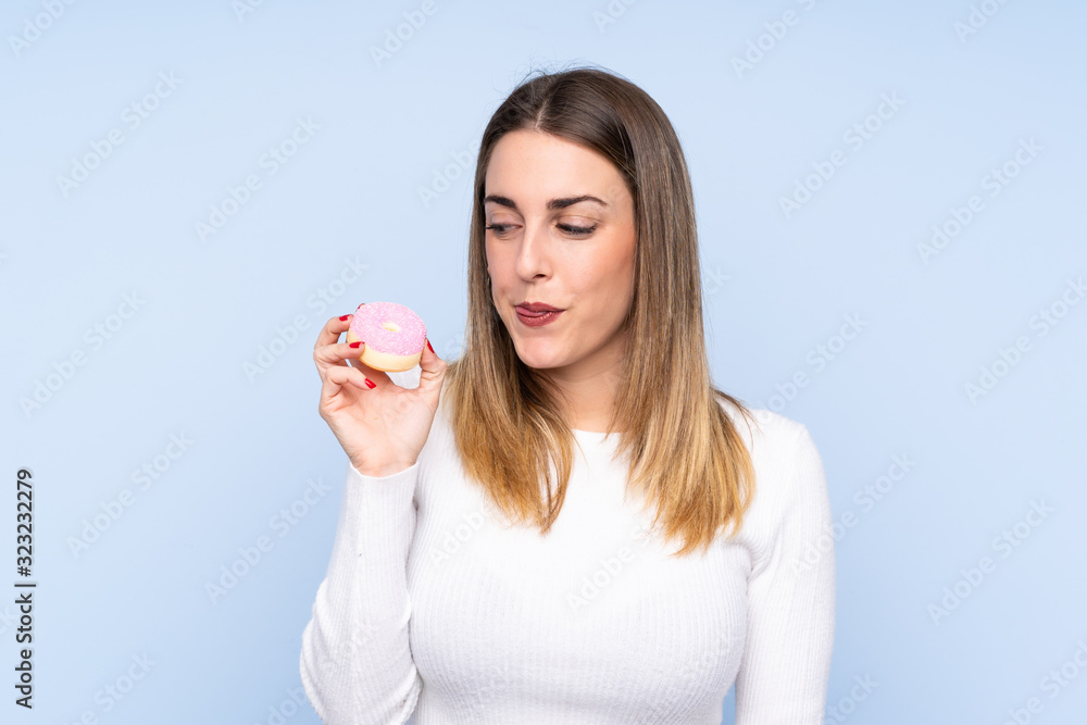 Young blonde woman over isolated blue background holding a donut Young blonde woman over isolated blue background holding a donut