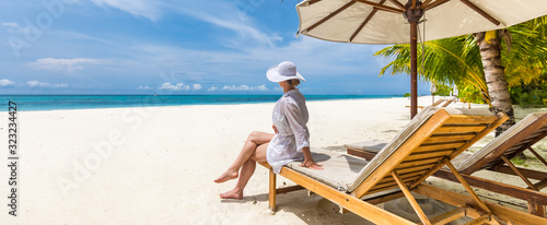 Fotografia Beautiful woman white beach dress sitting on sunbed lounges watching the calm sea