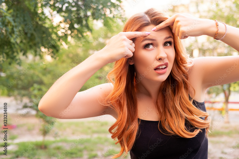 Beautiful plus size woman squeezing pimple on her forehead using her hands. Summer outdoor portrait, copy space