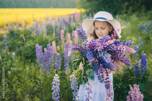 Beautiful girl in a dress and hat with a bouquet of flowers in the field