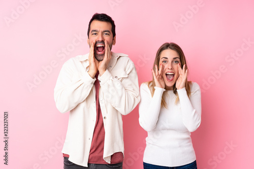 Couple in Valentine Day over isolated pink background shouting and announcing something