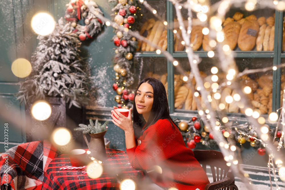 young beautiful brunette girl in a red sweater and white pants drinks tea on a street in Paris against the background of a window of a bread shop young beautiful brunette girl in a red sweater and white pants drinks tea on a street in Paris against the background of a window of a bread shop