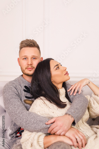 young beautiful couple, brunette girl in a white sweater, blond man sit on the bed in a bright room