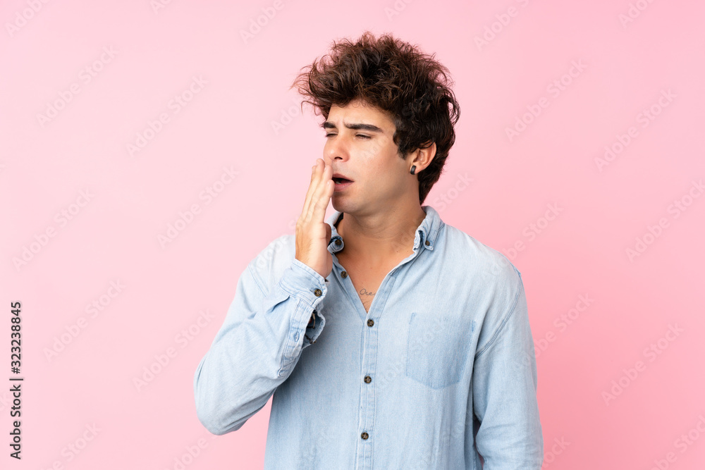 Young caucasian man with jean shirt over isolated pink background yawning and covering wide open mouth with hand Young caucasian man with jean shirt over isolated pink background yawning and covering wide open mouth with hand