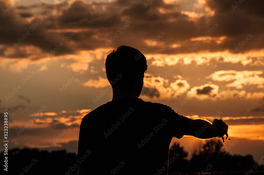 A silhouette of a man rsing his hands during a sunset.