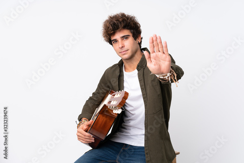 Young caucasian man with guitar over isolated white background making stop gesture with her hand