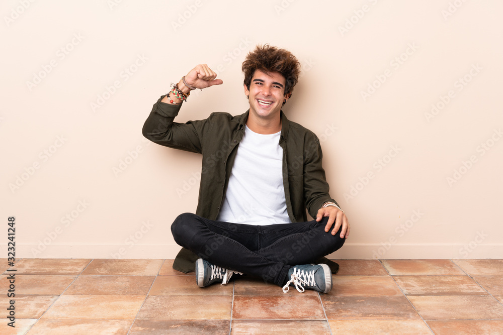 Young caucasian man sitting on the floor doing strong gesture Young caucasian man sitting on the floor doing strong gesture