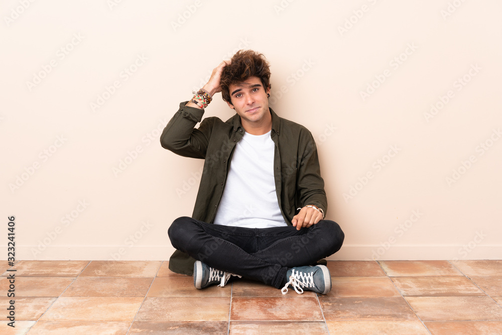 Young caucasian man sitting on the floor with an expression of frustration and not understanding Young caucasian man sitting on the floor with an expression of frustration and not understanding