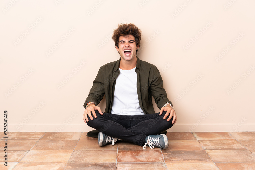 Young caucasian man sitting on the floor shouting to the front with mouth wide open Young caucasian man sitting on the floor shouting to the front with mouth wide open