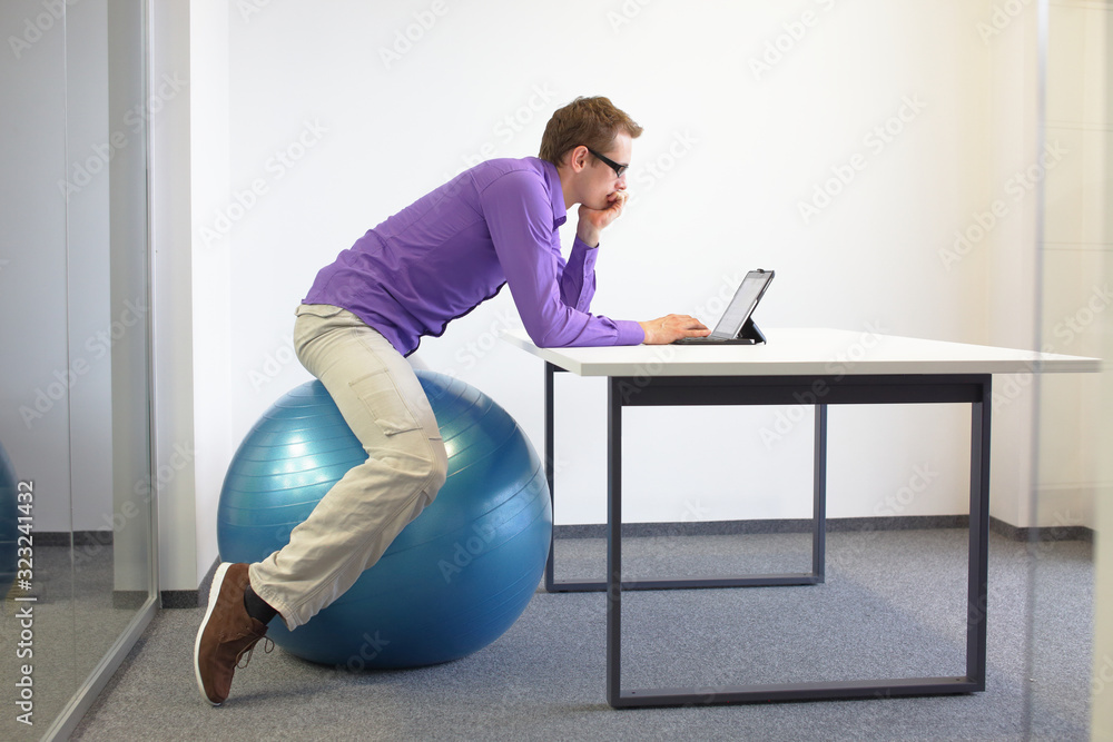 Man on stability ball working with tablet at desk in the office - changing siting position Man on stability ball working with tablet at desk in the office - changing siting position