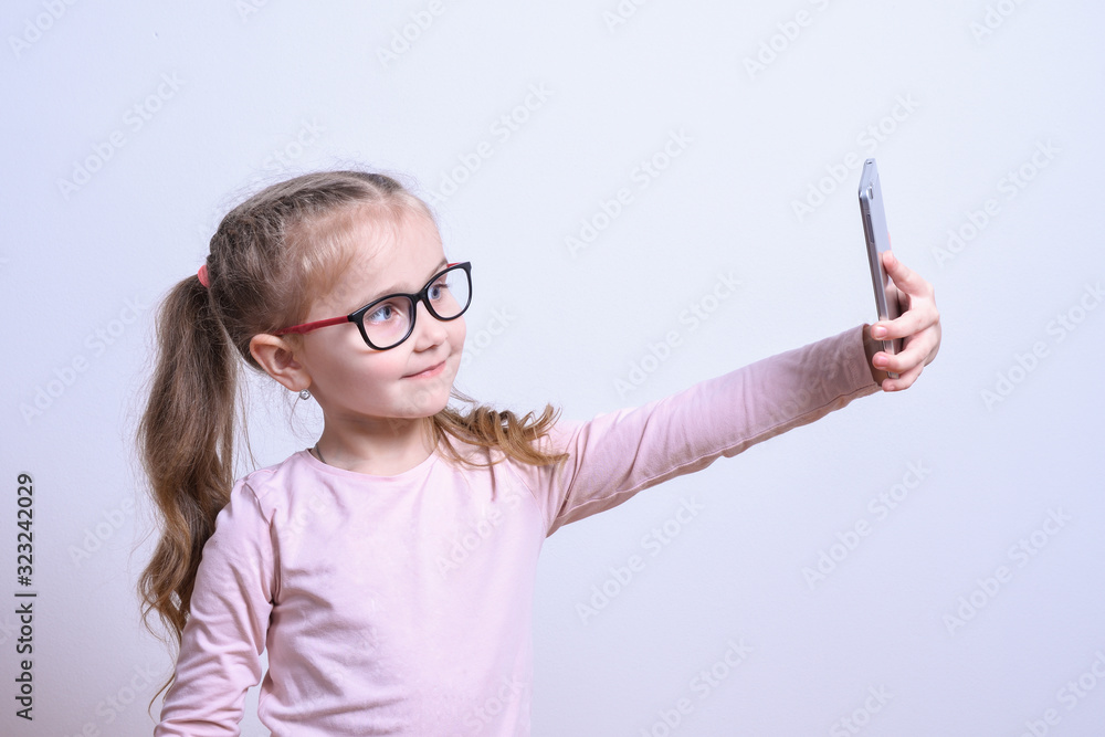Portrait of a little white girl make selfie on a mobile phone on a gray background Portrait of a little white girl make selfie on a mobile phone on a gray background