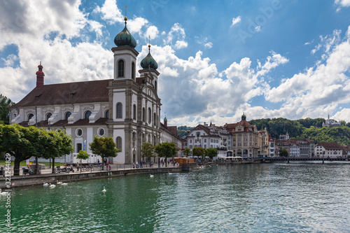 Panoramal view of the Lucerne Jesuit Church (Jesuitenkirche) on Reuss river side in old town of Lucerne with reflection in water, on a sunny summer day with blue sky cloud, Switzerland