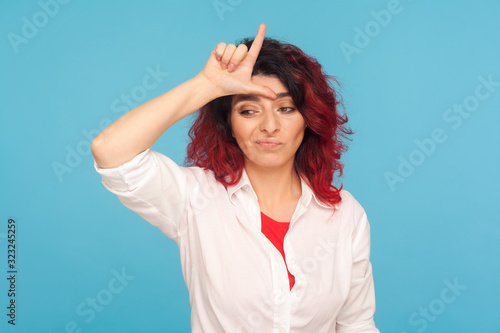 Obraz na plátně I'm loser! Portrait of unlucky depressed hipster woman with fancy red hair showing L sign on forehead, making loser gesture and feeling insecure, disappointed with defeat