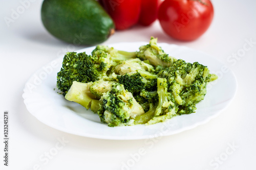 Plate with boiled broccoli, in the background vegetables red sweet pepper, tomato and avocado