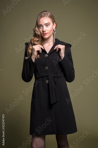 cute blonde model posing in a long black coat. standing. 