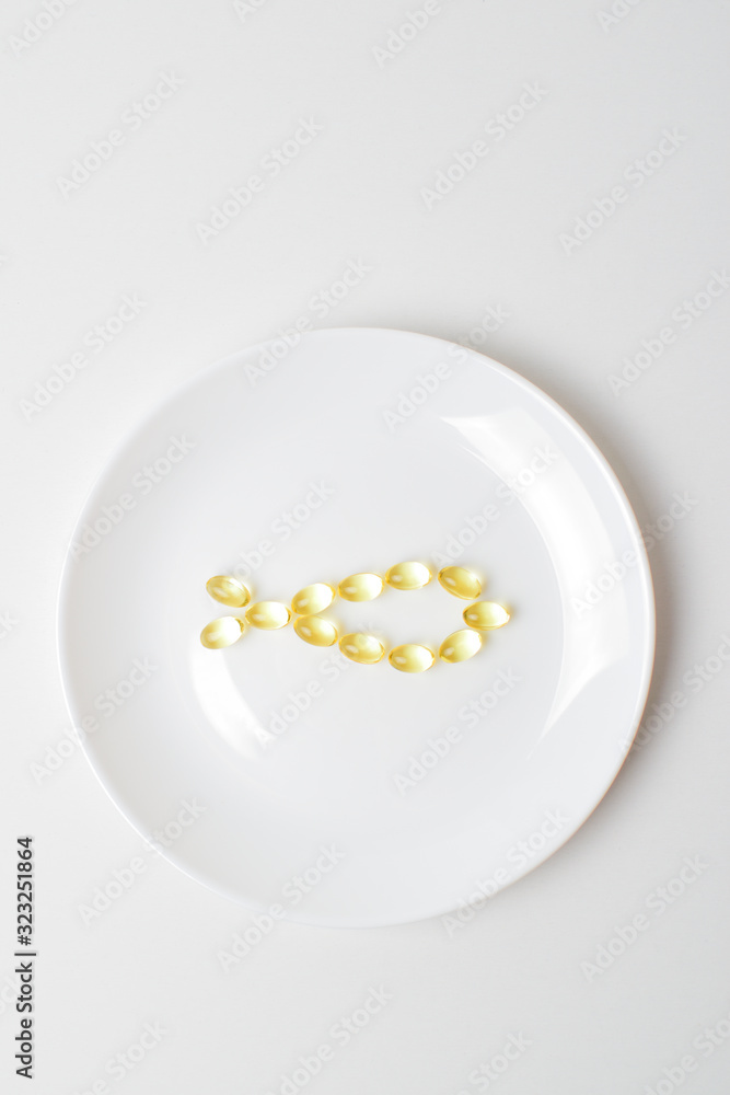 Fish oil softgels on a white plate in a shape of a fish. Meal replacement. Omega-3 polyunsaturated fatty acids on a plate. Casual nutrition prescription. Copy space above. Fish oil softgels on a white plate in a shape of a fish. Meal replacement. Omega-3 polyunsaturated fatty acids on a plate. Casual nutrition prescription. Copy space above.