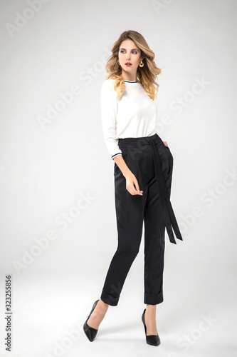 blonde model posing in her black chic pants and white blouse. white background. studio shot. standing. 