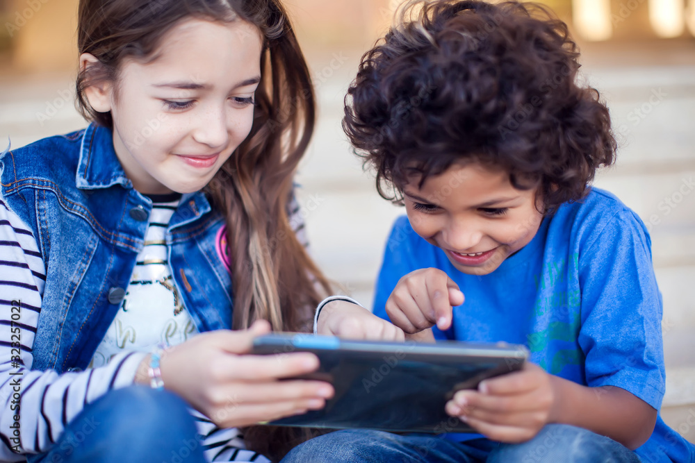 Two kids boy and girl playing with tablet outdoor. Children and gadget addiction concept Two kids boy and girl playing with tablet outdoor. Children and gadget addiction concept