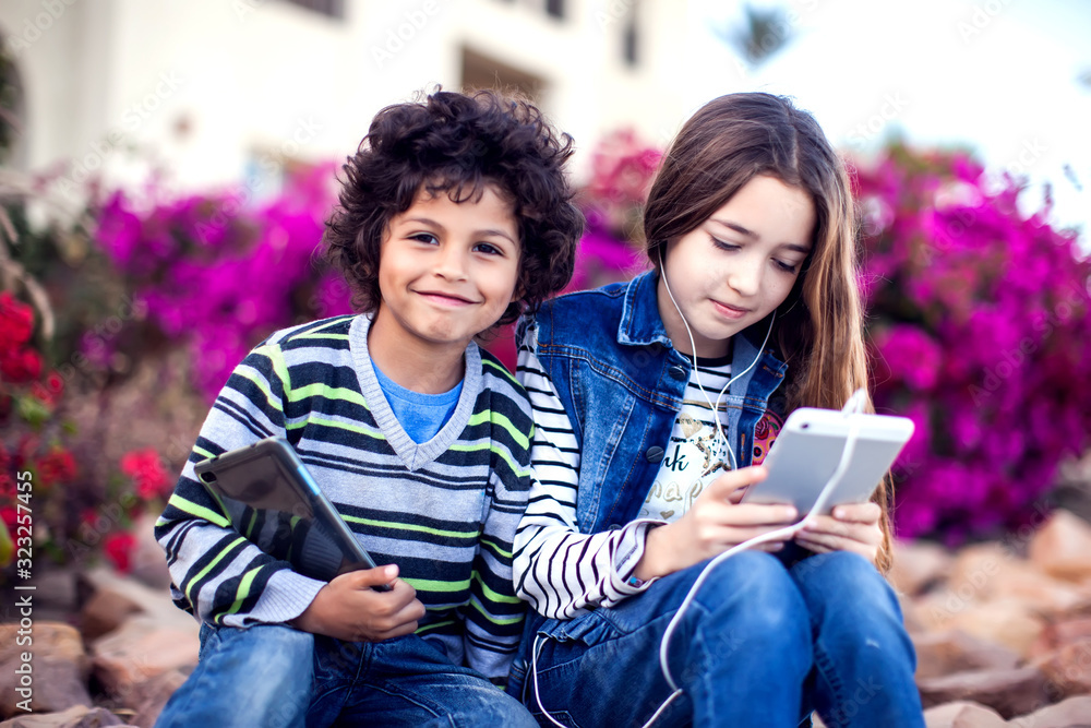 Two kids boy and girl playing with tablet outdoor. Children and gadget addiction concept Two kids boy and girl playing with tablet outdoor. Children and gadget addiction concept