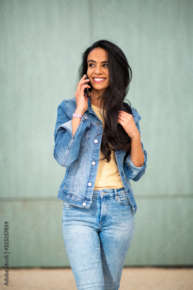 attractive young woman talking with mobile phone while walking by green wall