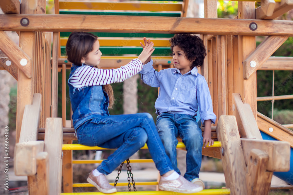 Two smiling kids friends boy and girl sitting on playground outdoor. Childhood and friendship concept Two smiling kids friends boy and girl sitting on playground outdoor. Childhood and friendship concept
