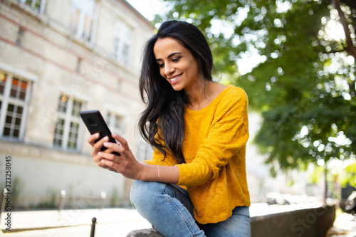 smiling young North African beautiful woman sitting outside in city looking at mobile phone
