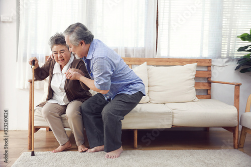 Couple elderly retirement husband helping wife have a back pain,with a walking stick to help him in the room at house. photo