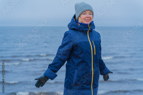 Portrait of middle-aged woman with her hands outstretched on a blue sea background. Cold winter day. photo