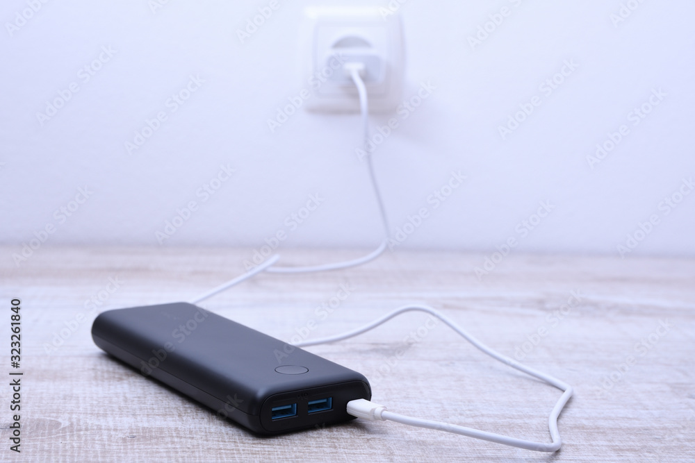 Black phone power bank plugged in the socket on the wall for charging on wooden background Black phone power bank plugged in the socket on the wall for charging on wooden background
