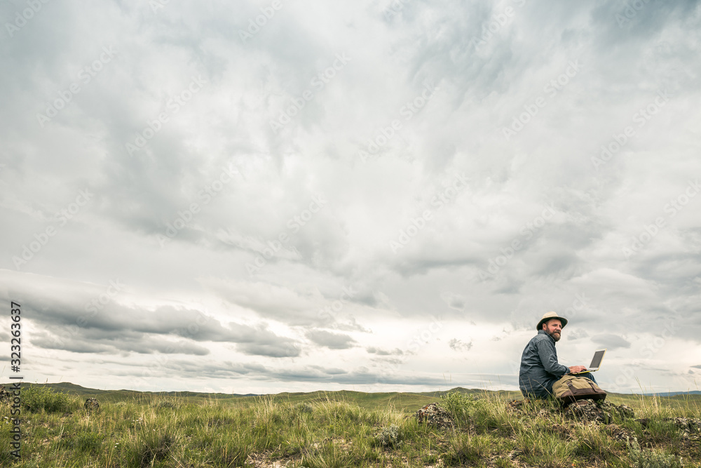 Bearded man working on laptop in rural prairie landscape. Cody, Wyoming, USA Bearded man working on laptop in rural prairie landscape. Cody, Wyoming, USA