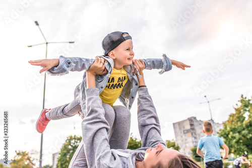 Woman mother parent playing with son, little boy child 4-5 years old, summer city. Rest on weekend. Emotions of tenderness caring parenting and love. Happiness fun and positive. A game of airplane. © byswat