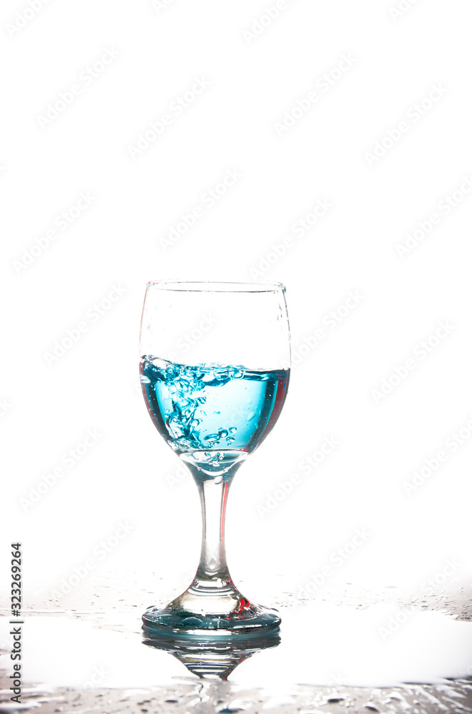 Splashing blue water into the crystal wine glass, closely spreading on a white background. Splashing blue water into the crystal wine glass, closely spreading on a white background.