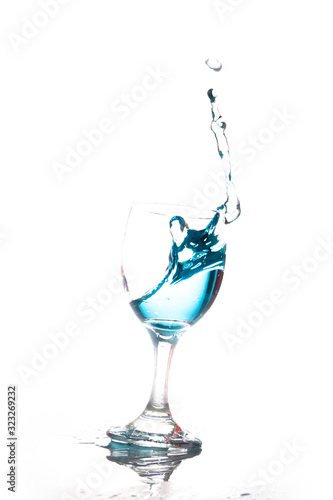 Splashing blue water into the crystal wine glass, closely spreading on a white background.