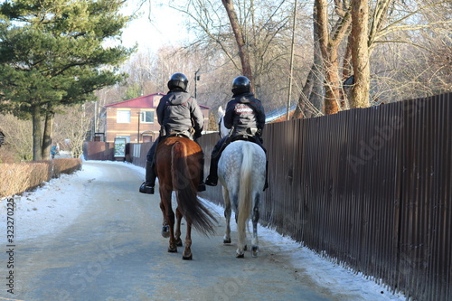 Two mounted police officers in uniform are driving along the road in the Park. The view from the back. The photo was taken in natural daylight.
