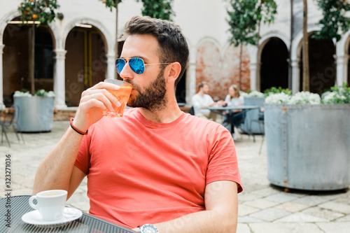 Young handsome man sitting in an outdoor cafe in summer time drinking coffee and cocktail