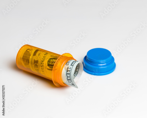 Prescription drug, medicine pill bottle with 100 dollar bill inside isolated on white background. Concept of rising drug, health care, medical insurance cost