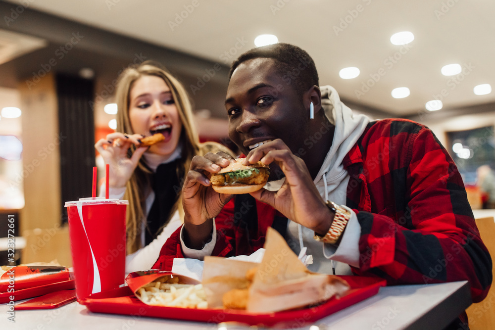 Young loving couple enjoying breakfast in burger bar,manbites a burger, woman eat chicken nuggets. Love, dating, food, lifestyle concept, st valentine's day.
