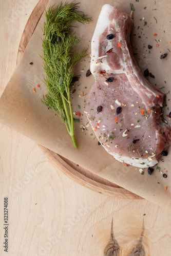 Pink raw pork steaks lie on a wooden board in spices and green dill. Appetizing meat. On craft paper and a wooden background. Yummy