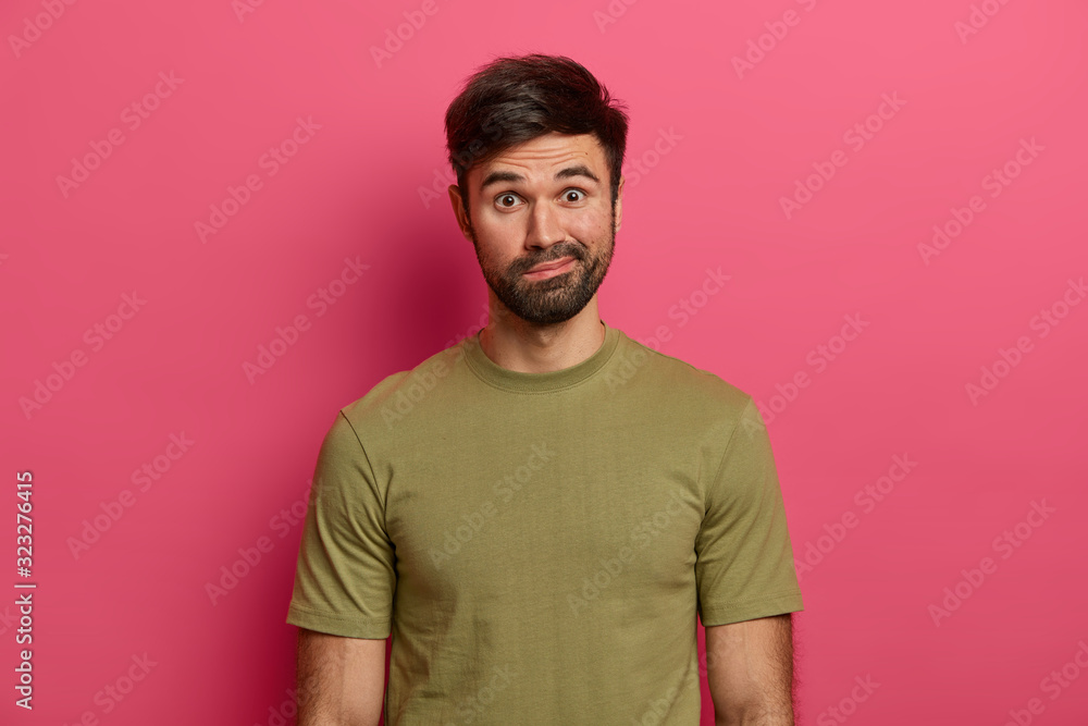 Indignant bearded Caucasian man purses lips, looks with wonder, sees something interesting, wears casual t shirt, isolated over pink background. Human facial expressions and emotions concept. Indignant bearded Caucasian man purses lips, looks with wonder, sees something interesting, wears casual t shirt, isolated over pink background. Human facial expressions and emotions concept.