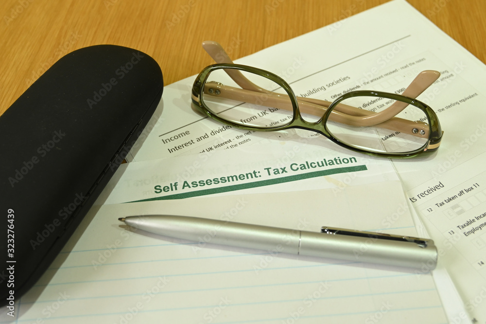 Close up view of a self assessment tax return form with a pen, a pair of glasses and a glasses case on a wooden table Close up view of a self assessment tax return form with a pen, a pair of glasses and a glasses case on a wooden table