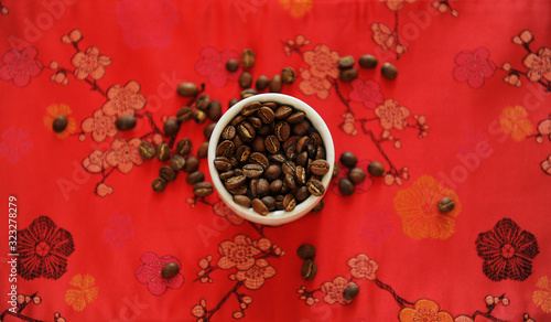 China specialty coffee concept. Roasted bean in white cup on red traditional chinese pattern fabric. Top view photo