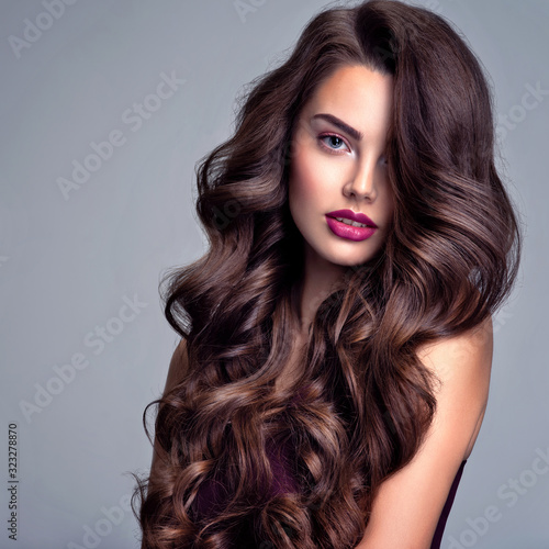 Face of a beautiful woman with long brown curly hair. Fashion model with wavy hairstyle. Attractive young girl with curly hair posing at studio. Female face with purple makeup. Violet make-up.