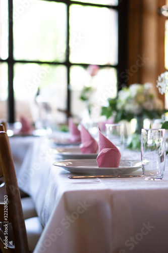 A beautiful set table with pink napkins and roses in the front of a sunny window photo