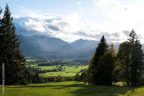 Sunny and overcast mountains in the background are frameed by some trees and some grass in the foreground photo